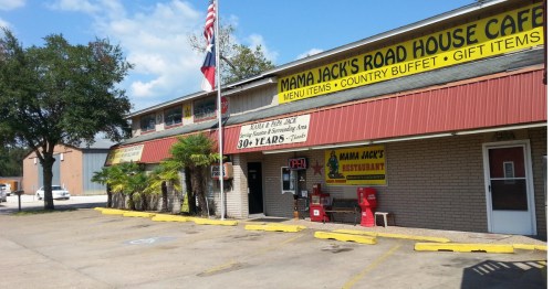 Exterior of Mama Jack’s Road House Cafe with a yellow sign advertising a country buffet and gift items, Texas and American flags out front, and a small parking lot.
