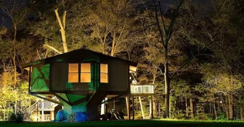 Rustic treehouse Airbnb cabin lit up at night, nestled among the trees for a unique, private forest getaway.