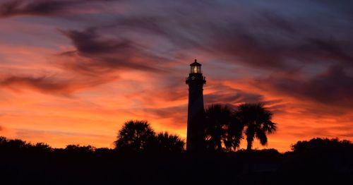 The St. Augustine Lighthouse at sunset, featuring a cloudy sky painted with swirls of purple, amber, and warm hues.
