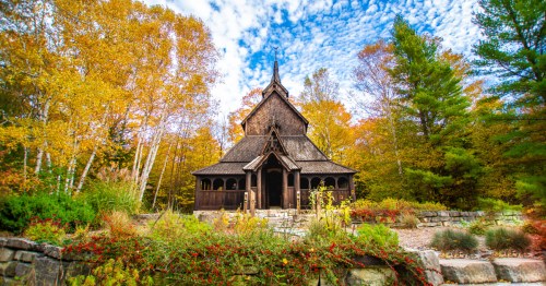 The Washington Island Stave Church surrounded by yellow and green fall foliage under a blue sky with spotty clouds
