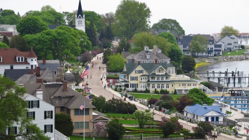 A scenic view of a waterfront town with lush greenery, historic buildings, and a pathway along the shore.