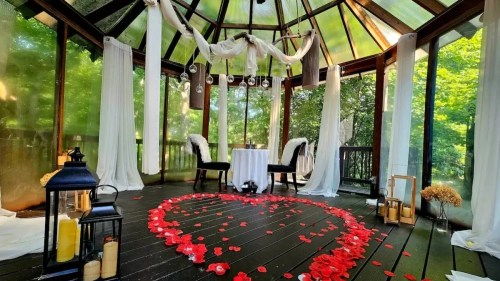 A romantic gazebo decorated with white drapes and a heart of rose petals on the floor, surrounded by soft lighting.