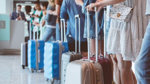 A line of travelers with suitcases waiting at an airport check-in counter.