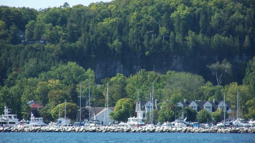 A scenic view of a marina with boats, surrounded by lush green hills and a clear blue sky.