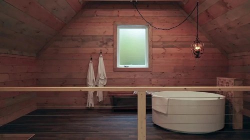Cozy wooden bathroom with a freestanding tub, two bathrobes, and a small window, featuring rustic decor.