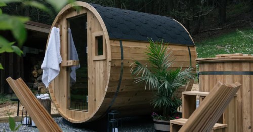 A cedar barrel sauna with a glass door and white towel on the handle at this wooded Connecticut Airbnb.