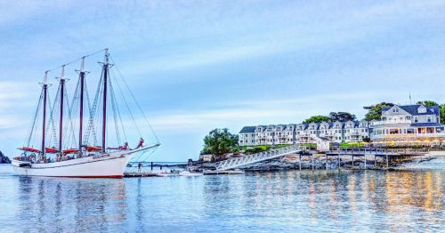 A scenic shot of Bar Harbor, where there's a ship sailing in the water and waterfront homes are aligned in the backdrop.