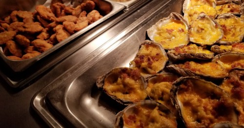 Buffet trays filled with crispy fried chicken and oysters topped with melted cheese and bacon bits.