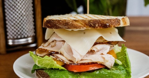 A club sandwich with fresh lettuce, tomato, deli turkey and thinkly sliced cheese on grilled bread, held together with a toothpick.