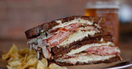 Halves of a grilled meat and cheese sandwich served alongside potato. chips