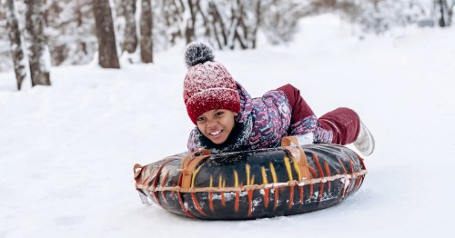 A girl wearing winter gear rides down a snow tube on your stomach.