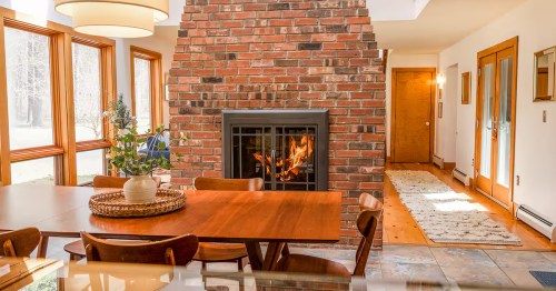 A brick, double-sided fireplace sits in back of a dining table and chairs at the Evergreen Home Airbnb property in Great Barrington, Massachusetts.