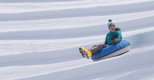 A snow tube rider sits in a blue tube and slides down a tubing hill at Gunstock Mountain Resort in Gilford, New Hampshire.