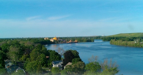 a bright blue body of water surrounded by green trees under the blue sky