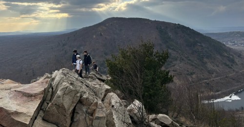 Hikers on a rocky ridge at Lehigh Gap summit with sun rays breaking through clouds in Pennsylvania.