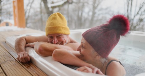 A couple relaxing in an outdoor hot tub with stocking hats on a cold winter day