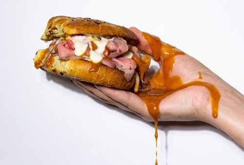 Person holding sandwich with sauce overflowing
