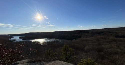 A view off a cliff into a landscape rich with lakes and forests as the sun begins to sink into the horizon.