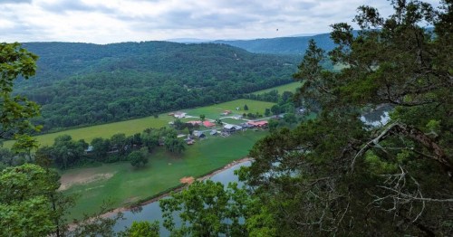 A bird's eye view of a river snaking through the small town of Mountain View, Arkansas, with rolling hills in the background.