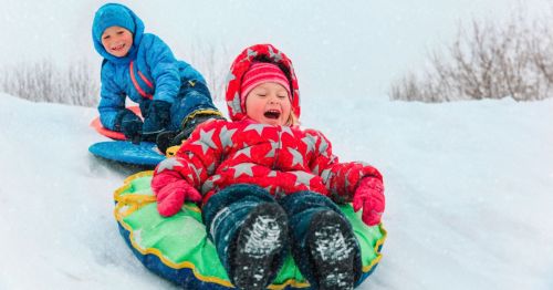 Two kids are having a fun winter day, laughing as they slide down a snowy hill in snow tubes.