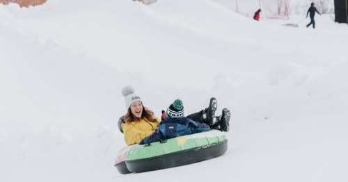 a woman and a child slide down a snowy hill on snow tubes at Bousquet Mountain in Massachusetts
