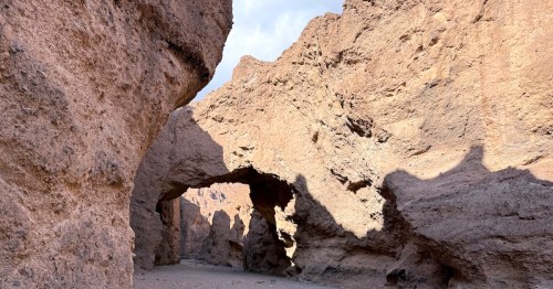 A detailed view of the rugged, sedimentary rock texture comprising the natural bridge arch as it connects the canyon walls under a blue sky.
