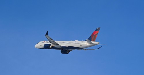A white Delta Air Lines passenger jet flies high through a clear, cloudless blue sky with its landing gear retracted.