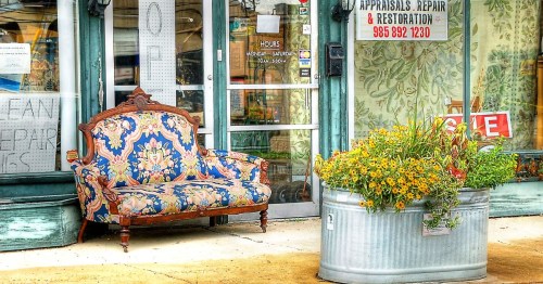 The entrance to an antique store in a dreamy small town in Louisiana, featuring a large planter with yellow flowers and a small antique sofa.