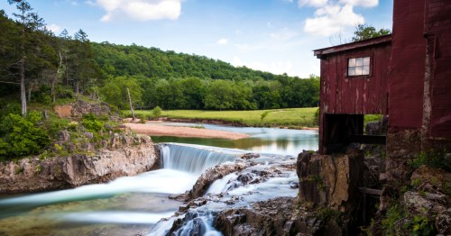 A red wooden mill along a flowing river in Eminence