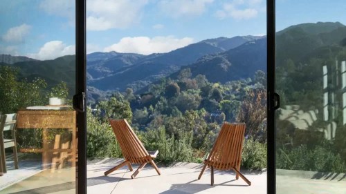 Two wooden chairs on a patio overlook a scenic mountain view under a clear blue sky.