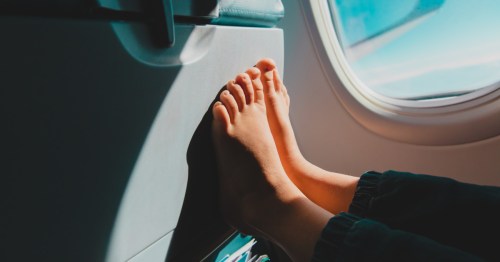 A person puts their bare feet on the tray table on an airplane.