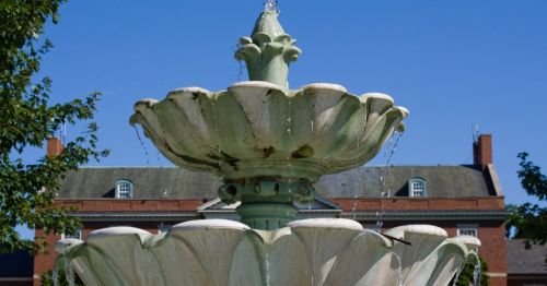 A close-up of a fountain with a brick building behind it.