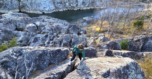 A hiker scaling up the side of a massive boulder along the Potomac River on an extreme hike in Maryland.