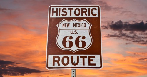 A brown and white sign for historic Route 66 New Mexico against a sunset sky.