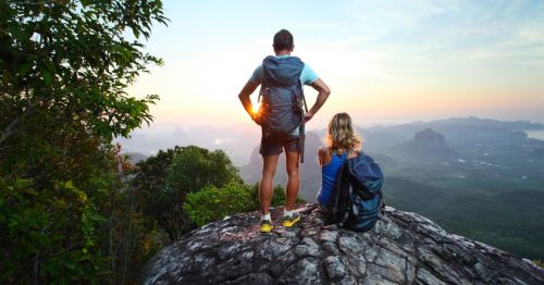 Two hikers perched on a large rock at sunset overlooking a scenic valley below.