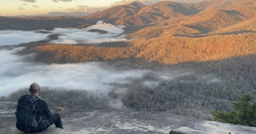 A man sits at the viewpoint of the Looking Glass Rock Trail in North Carolina.