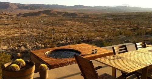 An outdoor hot tub overlooking a desert with a table.