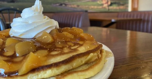 A stack of fluffy pancakes topped with fruit compote and a swirl of whipped cream.