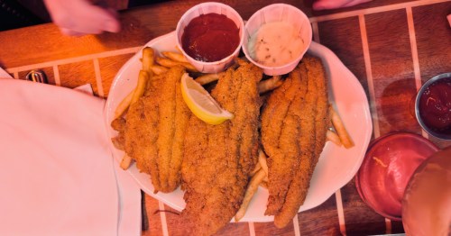 as seen from above, a white plate with fried catfish set on top pf french fries with a lemon wedge, ketchup, and tartar sauce at pappadeaux seafood kitchen in houston texas