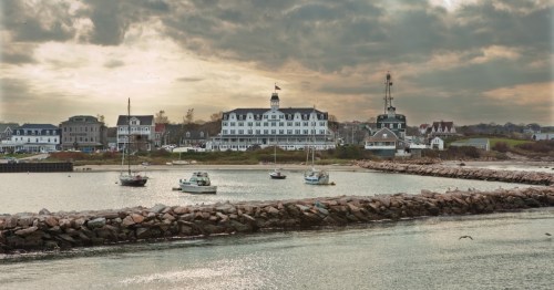 Dramatic stormy gold and grey clouds loom over a cute coastal town with boats bobbing in the ocean.