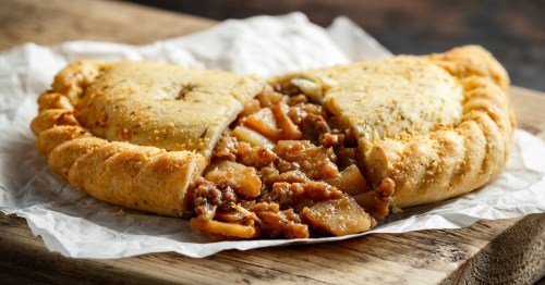 Traditional Cornish pasty filled with beef, potato and vegetables on black plate.