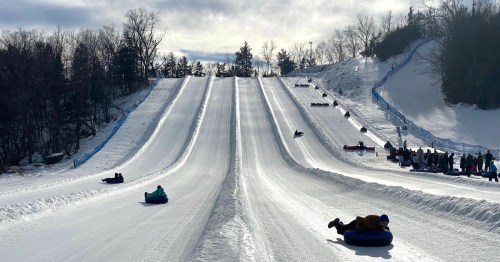 Snow tubers navigate down the multiple white runs at Seven Oaks, with a view of the lift lines and trees on either side.