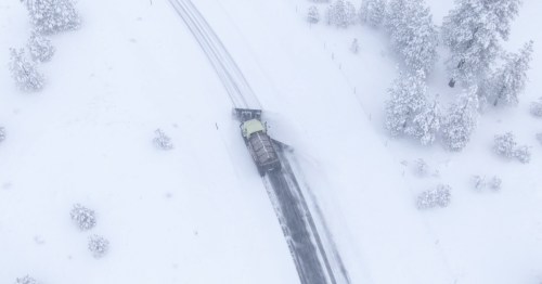 aerial shot of a snow plow plowing on a rural road during a winter storm