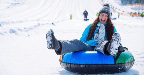 A woman dressed in blue rides a blue snow tube down a hill with a huge smile on her face.