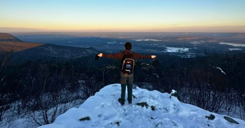 A man stands at the summit of the tallest mountain in Connecticut.