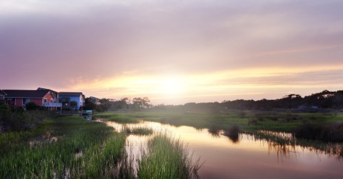The sun setting across the marshland with colorful houses framing the perimeter.