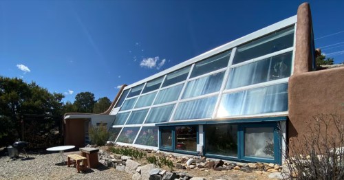 Sustainable Artsy Earthship in Taos, NM, featuring slanted glass windows and solar-integrated adobe architecture.