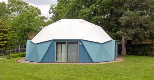 A round blue building with a white dome roof stands next to green trees.
