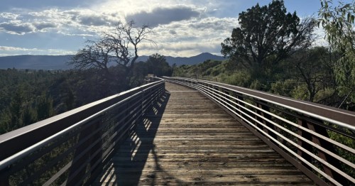 A paved walkway and bridge on the Los Alamos Canyon Rim Trail with mountain views.