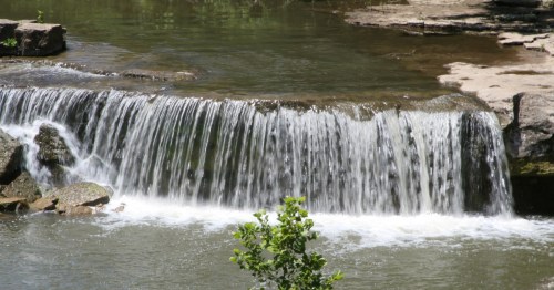 A wide, rushing waterfall cascading over a rocky ledge into a stream at Elk Falls, Kansas.